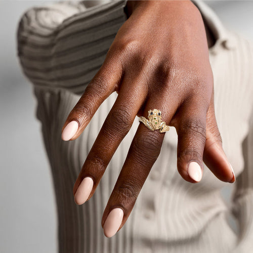 Gold frog ring worn on finger with blue and green stone details