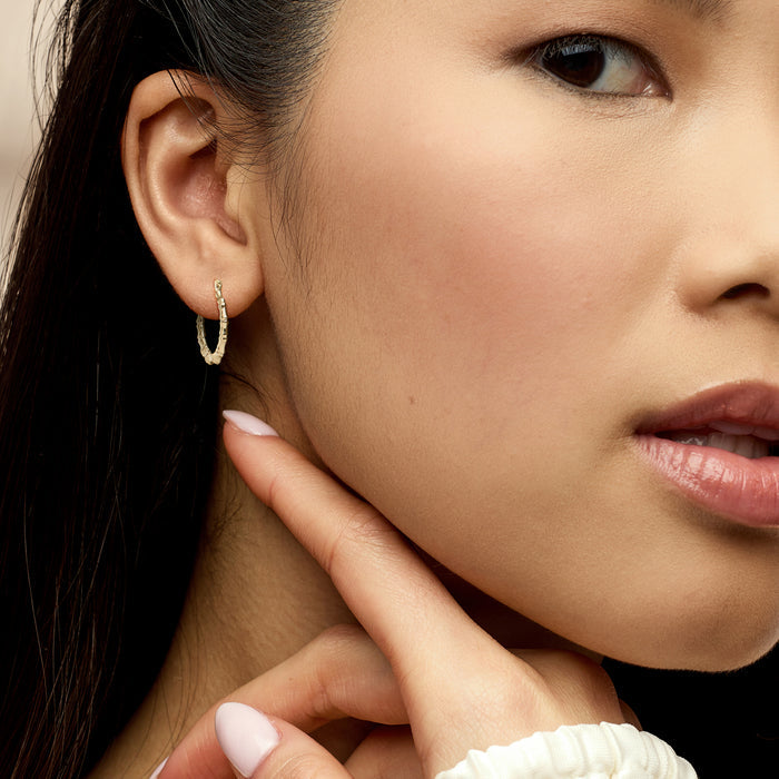 10kt yellow gold bamboo-style hoop earring worn on ear, textured bamboo look with hinge