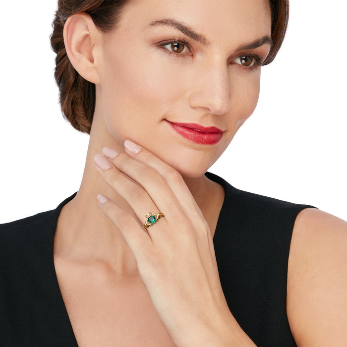 Gold-tone claddagh ring with green simulated gemstone worn on model's finger