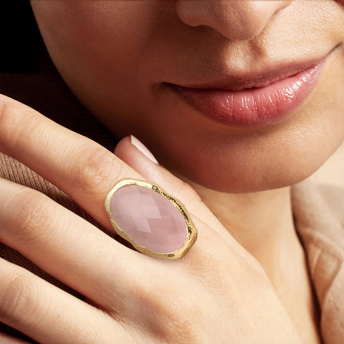 Rose quartz oval ring on finger, gold-plated bezel with faceted pale pink stone