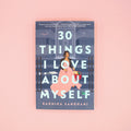A paperback copy of 30 Things I Love About Myself by Radhika Sanghani sits on a pink background.