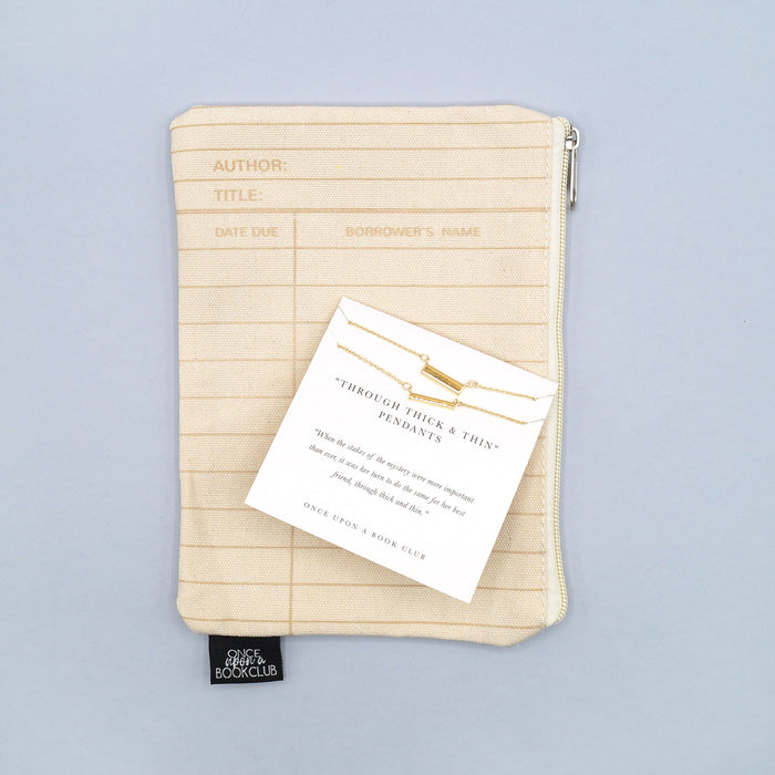 a beige library card patterned makeup bag with a set of two gold-plated bar necklaces on top, labeled "Through Thick & Thin Pendant"