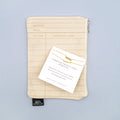 a beige library card patterned makeup bag with a set of two gold-plated bar necklaces on top, labeled "Through Thick & Thin Pendant"
