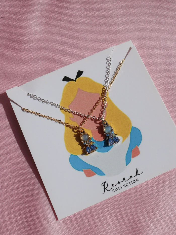 A gold-colored  Alice necklace with blue zirconia pendants, displayed on a pink background with a graphic of a character's head and the Reorah Collections logo.