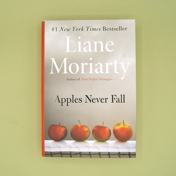 A hardcover copy of Apples Never Fall by Liane Moriarty sits on a green background.