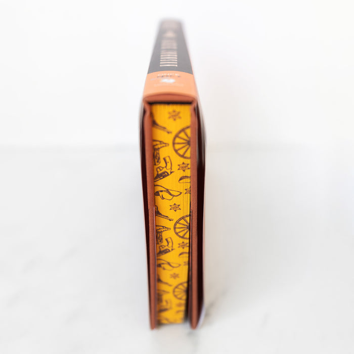 the custom stenciled edges of the Once Upon a Book Club exclusive edition of Bladestay by Jackie Johnson featuring a bright yellow background and multiple old west symbols including pistols, wagon wheels, sheriffs badges, cowboy hats, and cowboy boots.