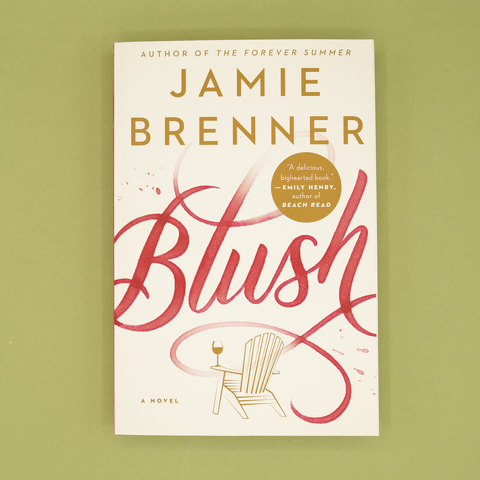 A paperback copy of Blush by Jamie Brenner sits on a green background.