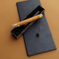 a tube of sandalwood incense sticks lays on top of an open box next to a small gold teardrop incense stick holder