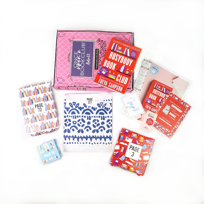 A paperback edition of The Busybody Book Club stands on a pink OUABC box. In front of the box are four themed wrapped gifts labeled with page numbers.