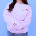 Person wearing a pink sweatshirt with a red embroidered book lover quote and bow against a blue background