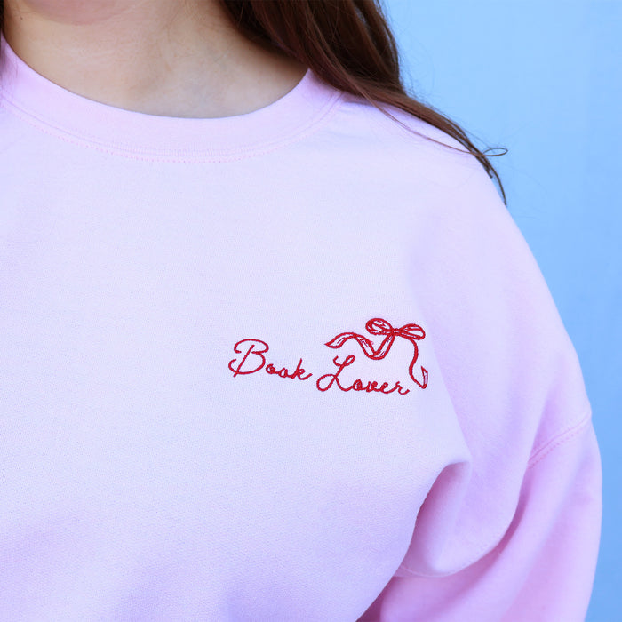 Pink sweatshirt with 'Book Lover' embroidery on a light blue background