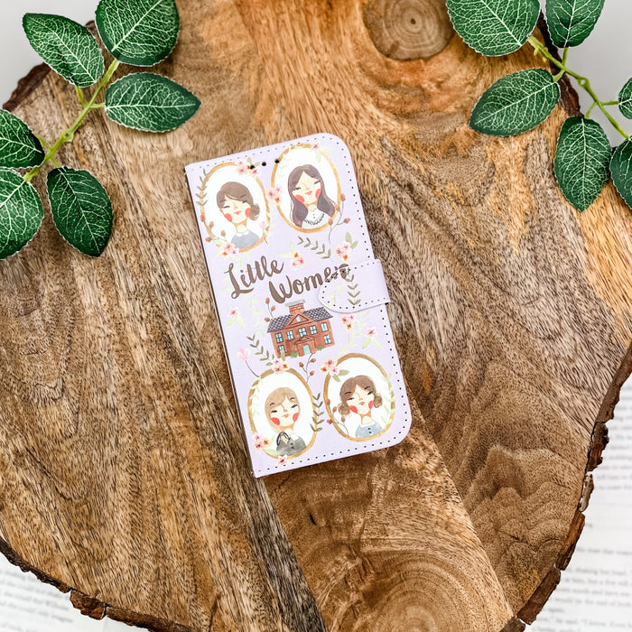 Little Women clutch with character illustrations on a wooden surface with green leaves.