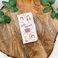 Little Women clutch with character illustrations on a wooden surface with green leaves.