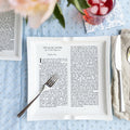 Dinner plate with The Great Gatsby text, set with cutlery on a patterned blue tablecloth.