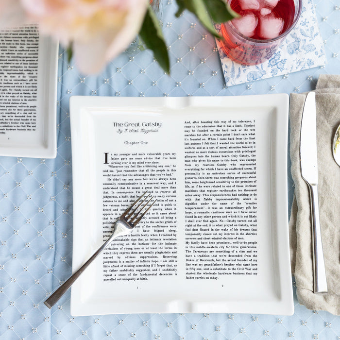 Dinner plate with The Great Gatsby text, set with cutlery on a patterned blue tablecloth.