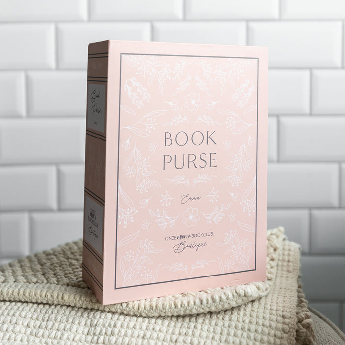 The book-shaped box used to package our book purse. The box is light pink and features the words "Book Purse" "Emma" "Once Upon a Book Club Boutique" on the front cover and spine with floral detailing surrounding it.