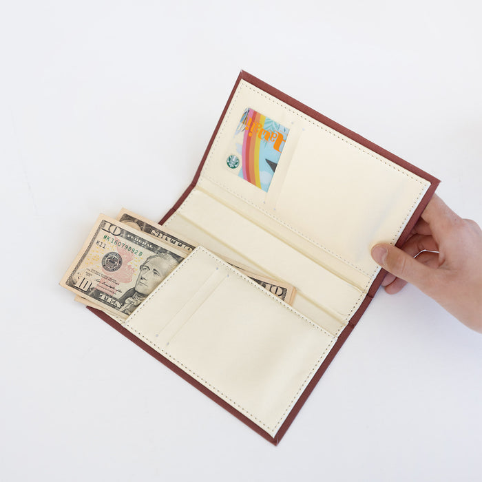 A white hand holds a red-brown wallet open, showing a beige interior with a gift card and cash tucked into the folds.