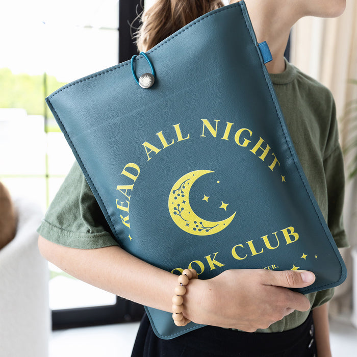 The "Read All Night" booksleeve is held in the arm of a reader as it protects their book inside.