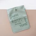 A booksleeve sits on a two-toned background. This booksleeve reads "When in doubt, read a book." in dark green font on a light green background and dark green floral details.