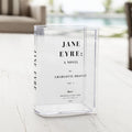 Clear acrylic vase styled as a "Jane Eyre" book cover, placed on a light wooden surface.