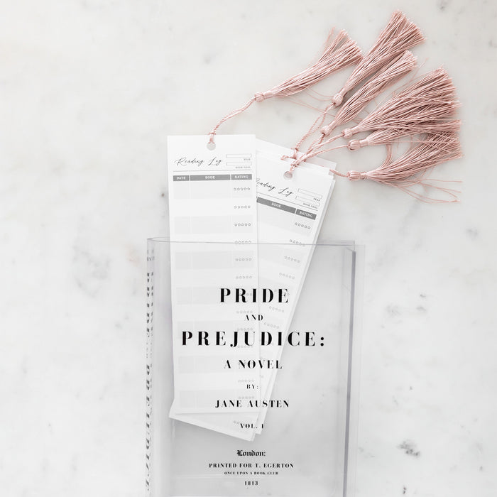 Clear vase with "Pride and Prejudice" design, holding pink-tasseled reading log bookmarks.