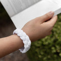 A hand holding an open book wears a white corded bracelet on their wrist.
