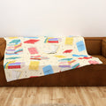 Colorful butter yellow book-patterned blanket on a brown couch against a white wall.