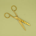 A pair of oversized, gold-toned scissors sits open on a green background.