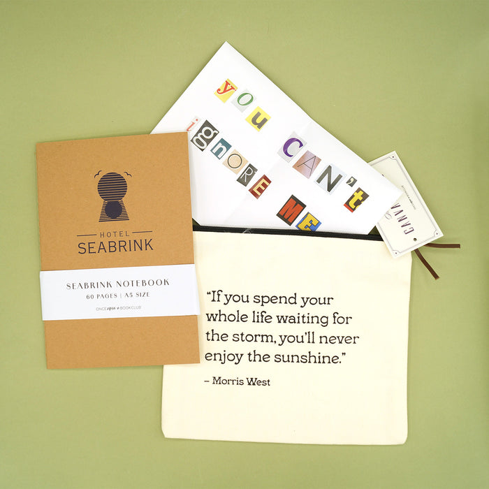A light brown notebook labeled Hotel Seabrink next to a white canvas bag with the quote If you spend your whole life waiting for the storm, you'll never enjoy the sunshine. - Morris West. A note with cut-out magazine letters is coming out of the bag that says 'you can't ignore me'.