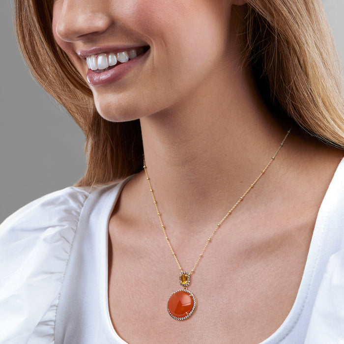 Gold-tone pendant necklace on model, featuring round orange gemstone with small yellow accent