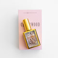 A gold perfume bottle labeled Cedarwood & Vanilla lays on a pink box.