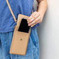 A light brown faux leather crossbody phone wallet with an iPhone half pulled out of it.