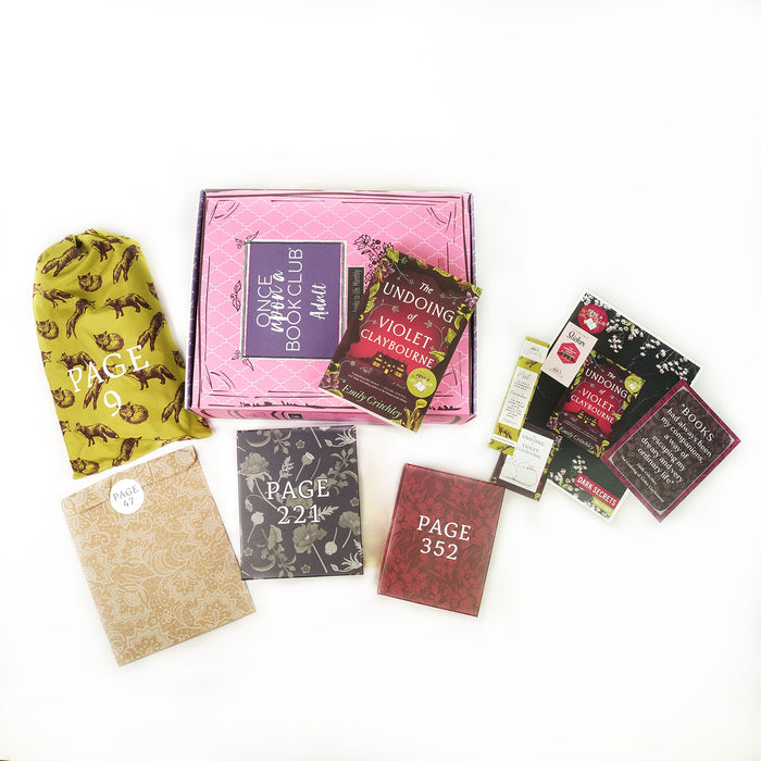 Paperback edition of The Undoing of Violet Claybourne lays on a pink box surrounded by wrapped gifts and paper items.