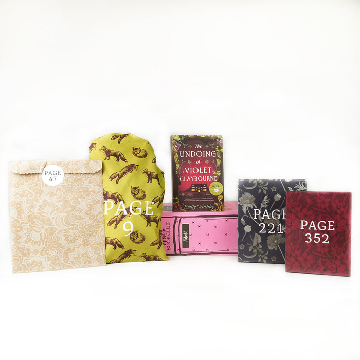 Paperback edition of The Undoing of Violet Claybourne stands on a pink box surrounded by wrapped gifts.