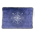 A dark blue fleece blanket with a swirl pattern and a white compass in the middle. The compass has two arrows pointing diagonally down, one southwest and one southeast.