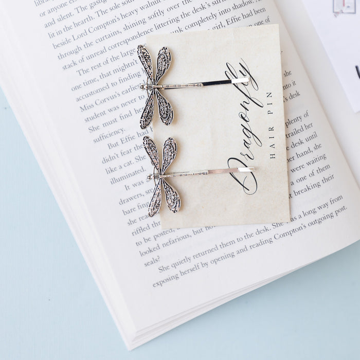 A set of two silver dragonfly-shaped hair pins lay on an open book