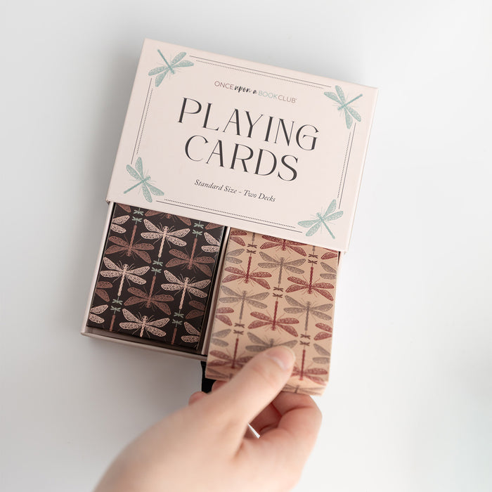 An open box showing two sets of standard size playing cards. The cards have a black and brown dragonfly pattern on their backs.