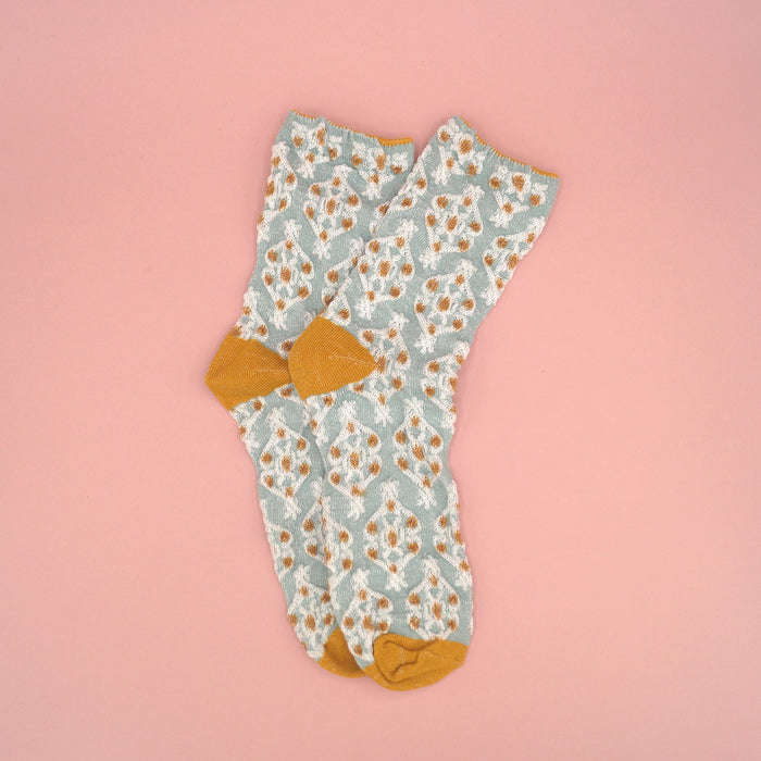 A pair of light blue socks with a gold and white pattern on them.