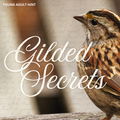 The September Young Adult hint image featuring a close-up photograph of a brown sparrow perched on a wooden surface, with large white script text reading 'Gilded Secrets' and smaller text 'YOUNG ADULT HINT' in the upper left. The background is softly blurred with warm neutral tones and faint cursive writing.