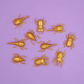 Ten fake golden beetles across a light purple background