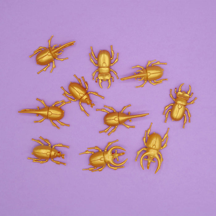 Ten fake golden beetles across a light purple background