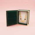 A double strand gold heart bracelet in a small book shaped box on a pink background.