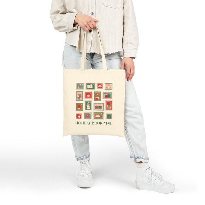 Person holding a beige tote bag with 'Holiday Book Mail' design on a white background