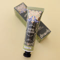 An olive green tube of Honey & Black Currant Hand Cream - Once Upon a Book Club. There is a floral pattern on the tube with two blue and white butterflies over the words. The tube lays against a matching box.