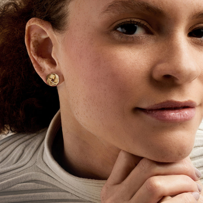 Gold love-knot stud earrings on model with textured swirl knot detail