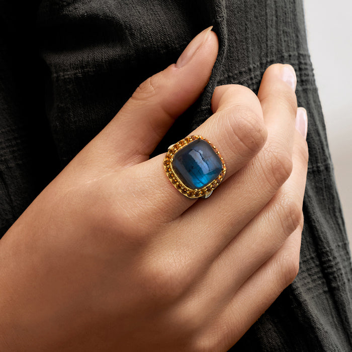 Gold-tone ring on hand featuring oval labradorite cabochon and orange citrine halo