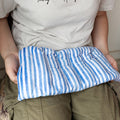 Hands hold a blue and white striped heating pad in her lap.