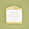 A bar of lemon & honey cleansing soap on a green background.