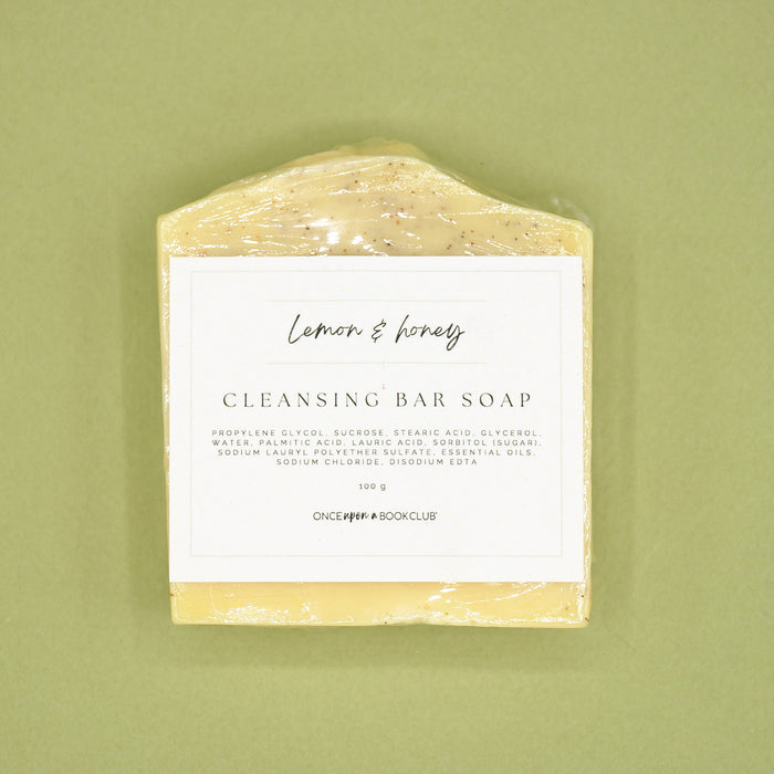 A bar of lemon & honey cleansing soap on a green background.