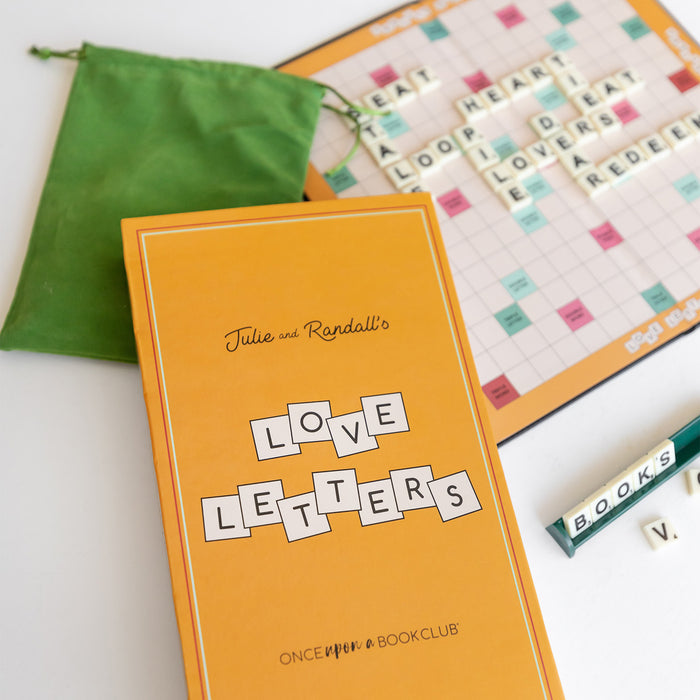 A box in the foreground is labeled Julie and Randall's Love Letters - Once Upon a Book Club. In the background is an open game board with letter tiles spelling out words.